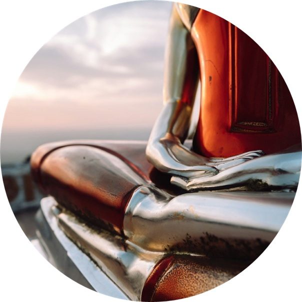 Bewusstseinsabend Detailaufnahme einer metallischen Buddha Skulptur mit einem Blick auf die Landschaft im Hintergrund.