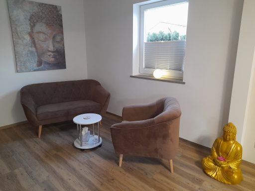 Beratung Gemütliche Sitzecke mit braunem Sofa, Sessel, Tisch, Buddha-Figur und Wandkunst.