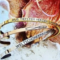 Dein Mantra Drei Armeifen mit Mantra-Gravur auf buntem Hintergrund.